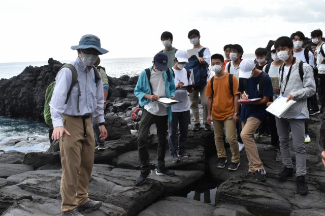 遠藤さん（左）の説明を聞く韮山高の生徒たち＝伊東市の城ケ崎海岸