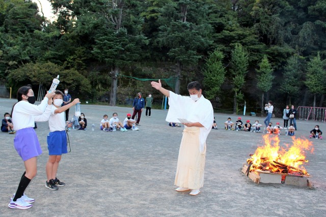 キャンプファイアで火の神様（右）から火を授かり、ＬＥＤランタンを点灯する児童＝熱海市の桃山小