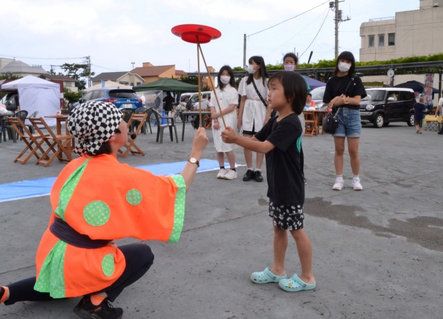大道芸人（左）と一緒に皿回しを体験する子ども＝伊東市渚町の松川藤の広場