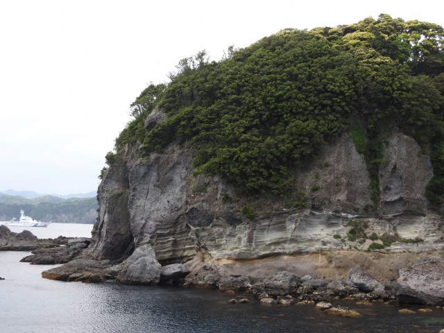 赤崎から見た州佐里崎（バンダリア岬）。断崖絶壁の中央下に地層の帯が確認でき、海底火山の噴出物の堆積層か。この上に台場遺跡と日本軍の監視用洞窟がある