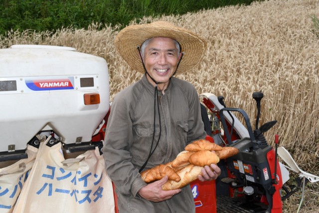 収穫前の小麦畑で手作りパンを手にする石川さん＝伊東市十足