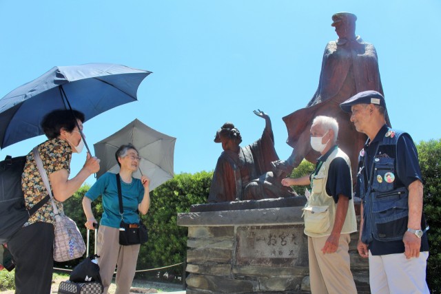 貫一お宮の像の前で解説する（右から）北島さんと田中さん＝熱海市東海岸町