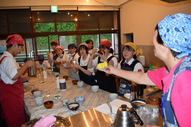 炊きたての黄飯を味わいながら、清水さん（右）が手にする小さなおにぎりを見る生徒たち＝東伊豆町稲取のダイロクキッチン