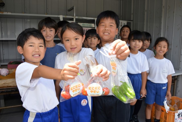 収穫して小袋に入れて販売する夏野菜を自慢げに披露する子どもたち＝下田市吉佐美のわんさ花（写真の一部を加工しました）
