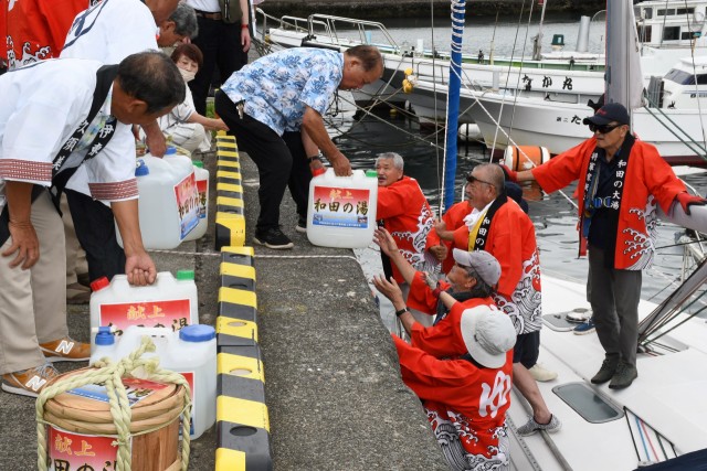 献上する「和田の湯」をヨットに積み込む実行チームのメンバーら＝伊東港