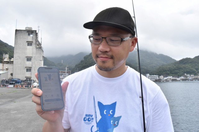 アプリ「海釣りＧＯ」を紹介する国村さん＝西伊豆町田子の田子漁港