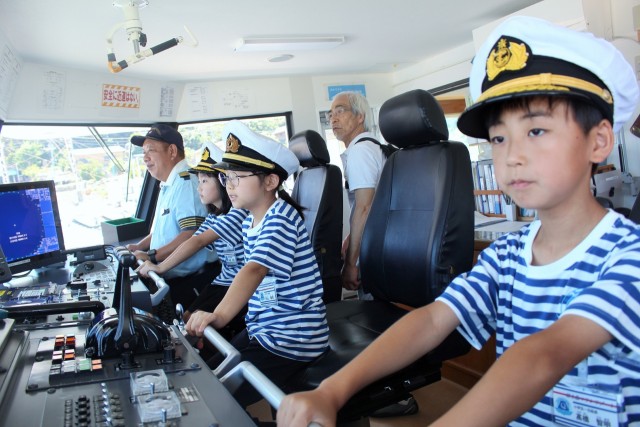 操舵室で普段船長たちが座る席に座る「小学生船長」の３人＝熱海市初島