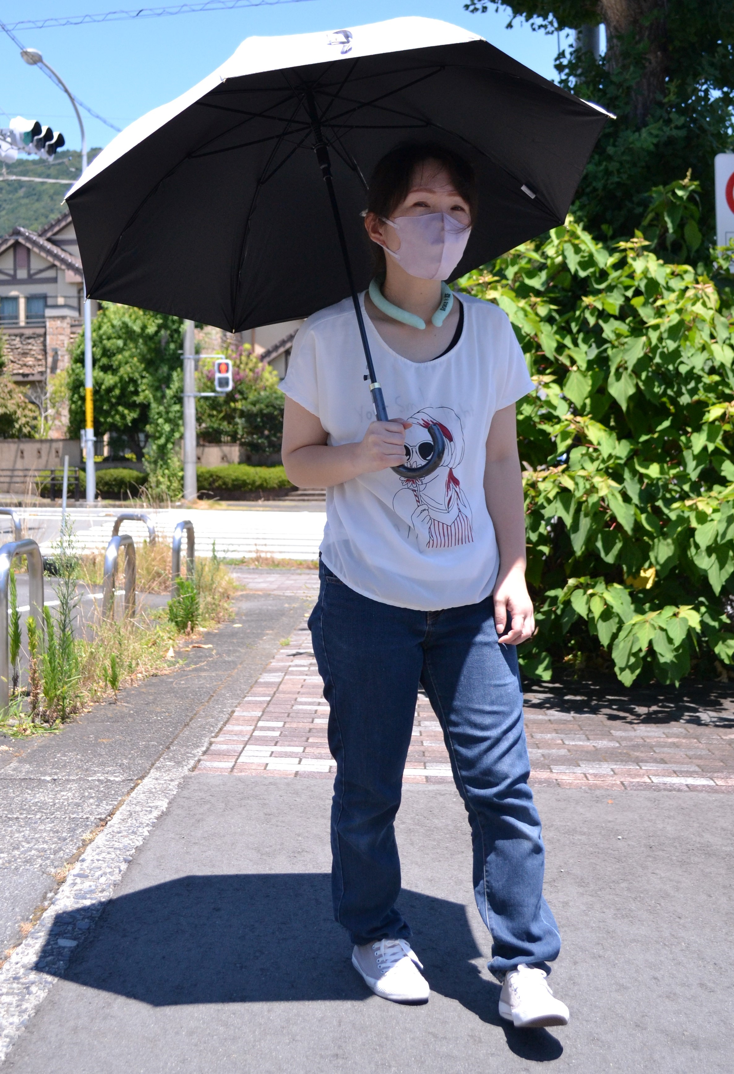 日傘をさし、首元を冷やすリングを付けて歩く女性＝伊東市内