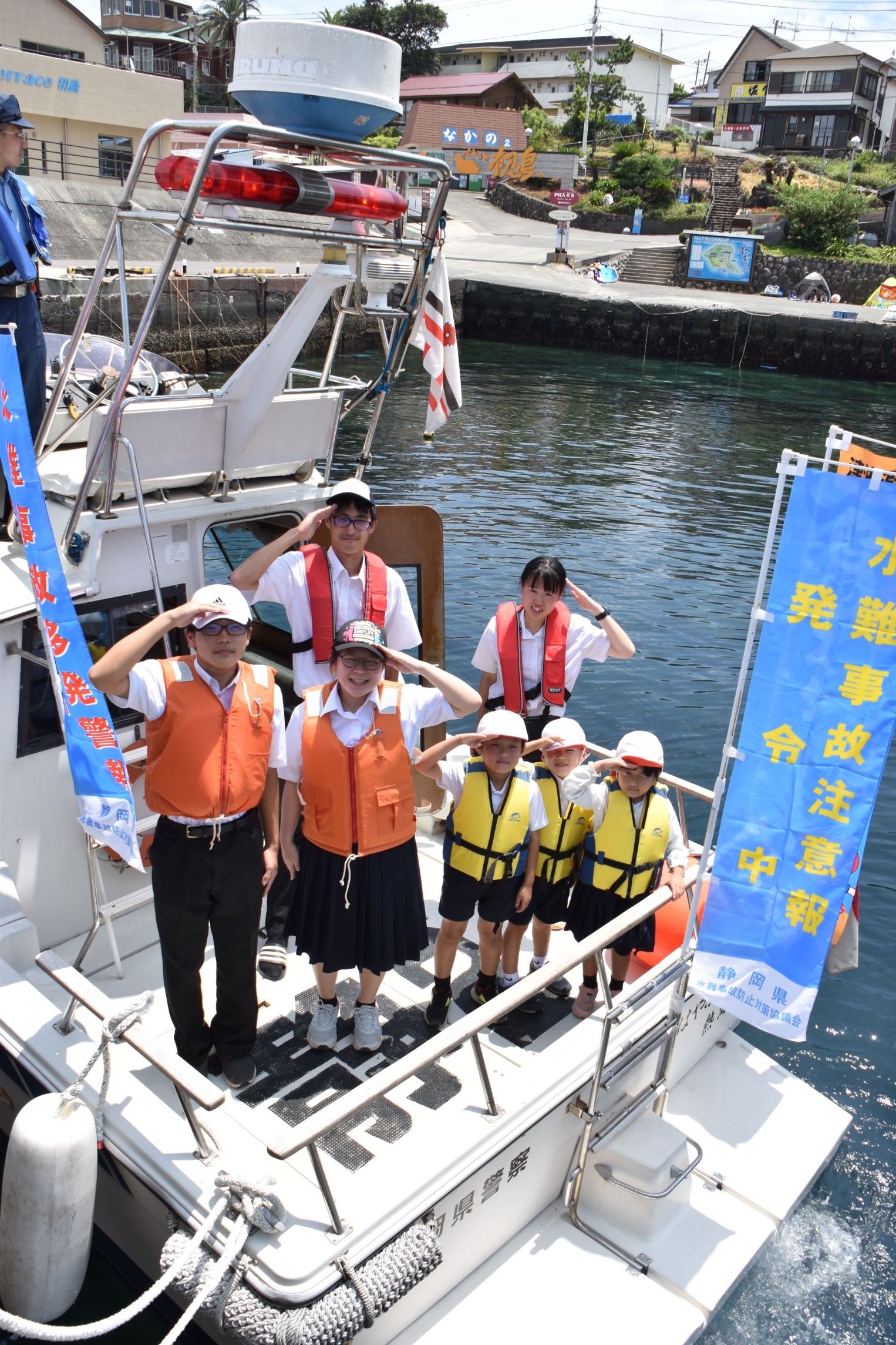 熱海署との合同海上パトロールで警備艇に乗り込み敬礼する初島小中の生徒児童ら＝熱海市初島の初島漁港（７月２１日）