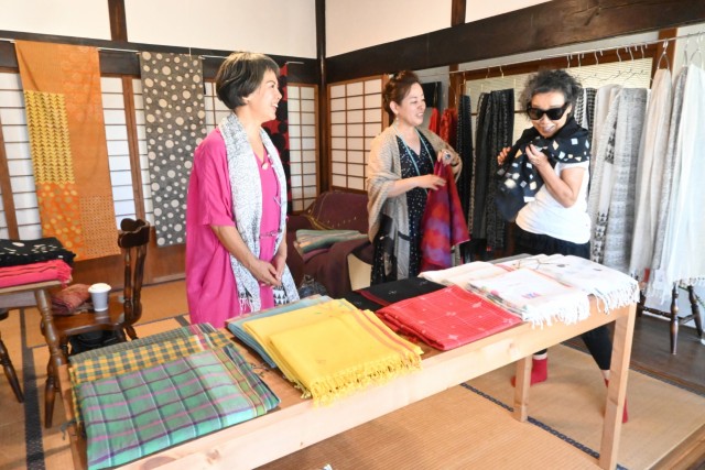 ストールを試着する来場者に織りの技法を説明する吉野さん（左）＝伊東市赤沢の「エーヨン」