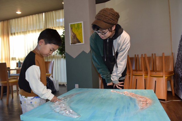 国司さん（右）が手がけたワニをモチーフにした作品に触れる子ども＝東伊豆町の熱川バナナワニ園分園