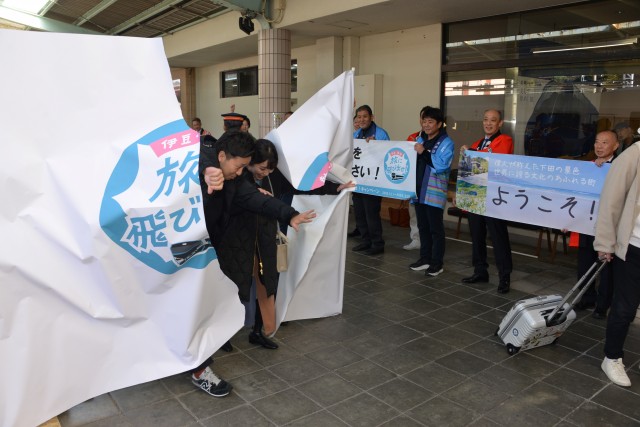 キャンペーンの歓迎幕を破って下田に一番乗りしたカップル＝下田市東本郷の伊豆急下田駅