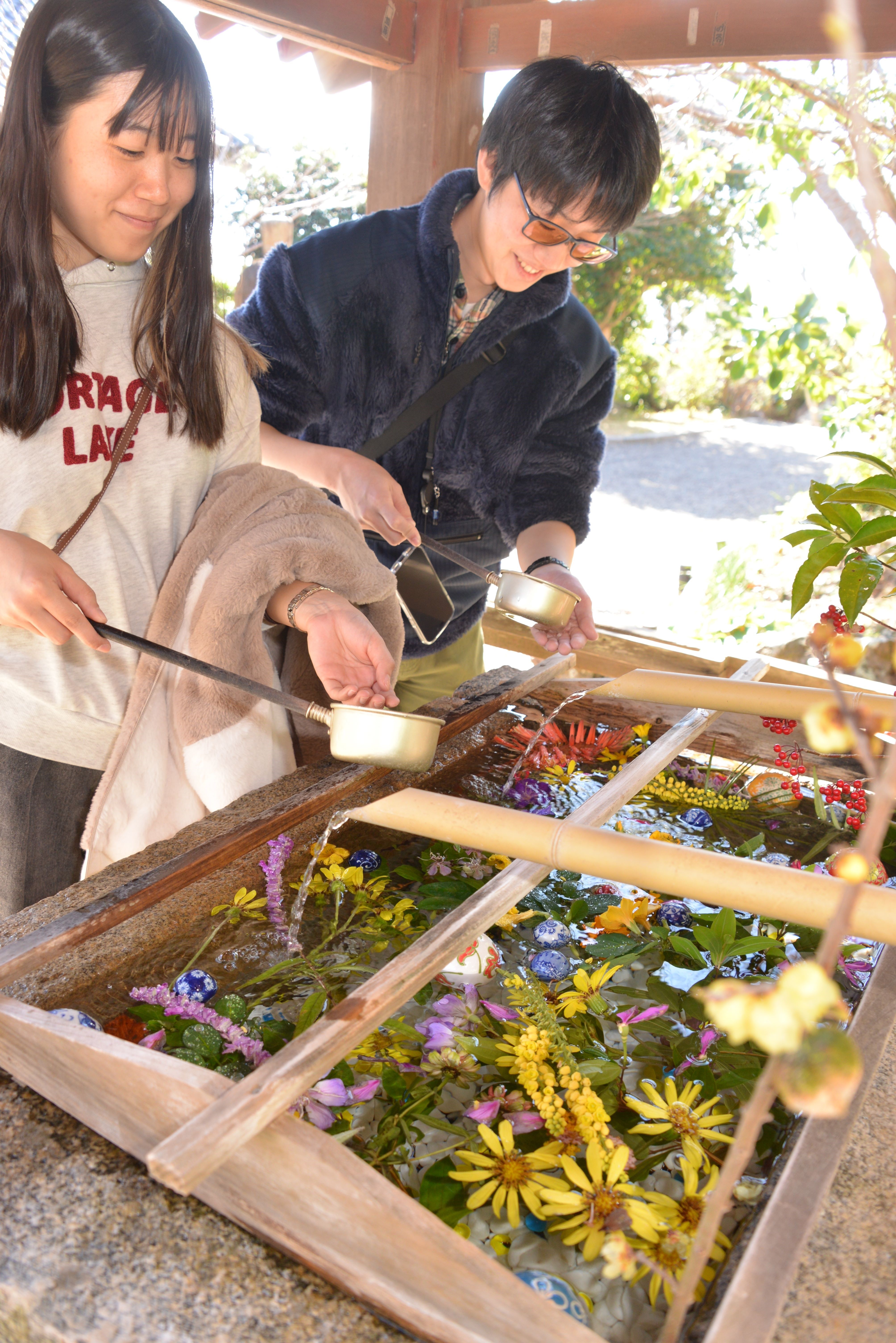季節の花で彩られた花手水で手を清めるカップル＝下田市の寝姿山公園愛染明王堂
