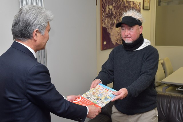 高橋教育長（左）に絵本を手渡すトドロキさん＝伊東市役所