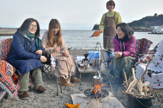 流木でたき火をして湯を沸かす参加者と菊地さん（右から２人目）＝伊東市の川奈いるか浜