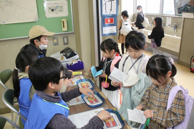 仕事を終えて銀行係（左側）から給料を受け取る子どもたち＝伊豆の国市の韮山生涯学習センター