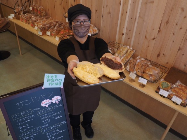 ずらりとパンが並んだ店内で、具材を塗ったサンドパンを手にする遠藤店長＝熱海市清水町