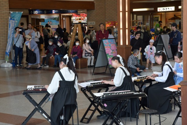 大勢の駅利用者を前に大正琴を演奏する子どもたち＝伊東市八幡野の伊豆高原駅