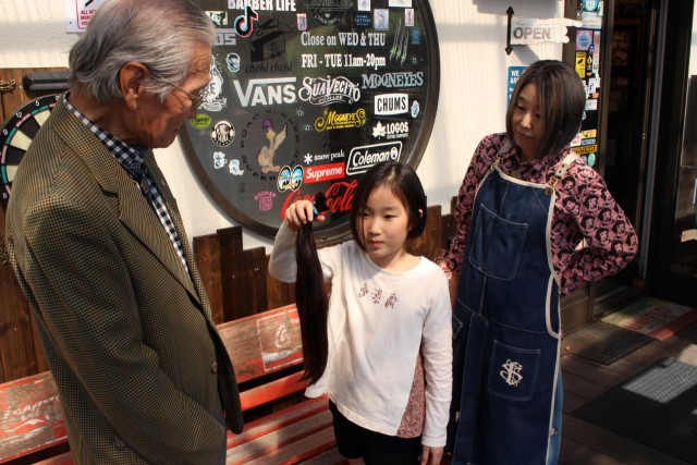 大仁ＬＣの土屋さん（左）に切った髪の毛を渡す飯田さん＝函南町上沢のカットハウスチョキチョキ