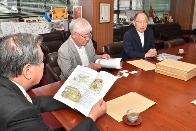 豊岡市長（左）に冊子を披露し説明する山形さん（中央）と一藤木さん＝三島市役所