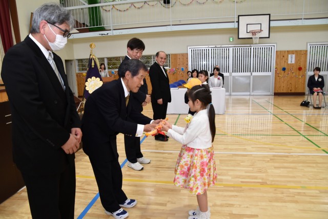 新入学児童代表に傘を手渡す石井会長（左から２人目）＝伊東市の富戸小
